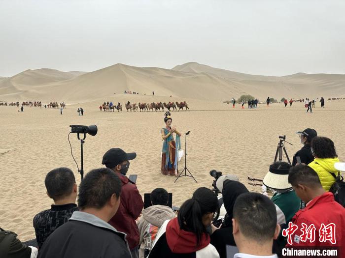 圖為2023年4月底，敦煌大漠“逐舞者”奧楠在鳴沙山月牙泉景區視頻直播，吸引游人圍觀。　馮志軍 攝
